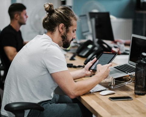 man holding turned-on iPad in front of turned-off MacBook Air