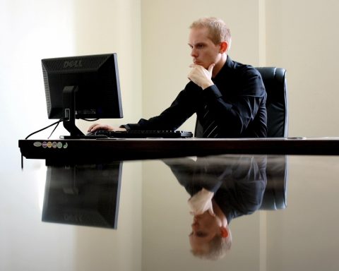 Man die peinzend achter zijn bureau zit en naar zijn laptop staart